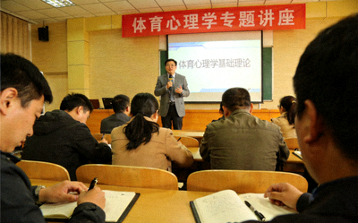 体育心理学讲座现场，讲师在台上讲解，台下听众认真听讲并做笔记